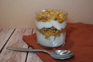 Cinnamon, granola, apples, and yogurt layered in a glass cup with a spoon 